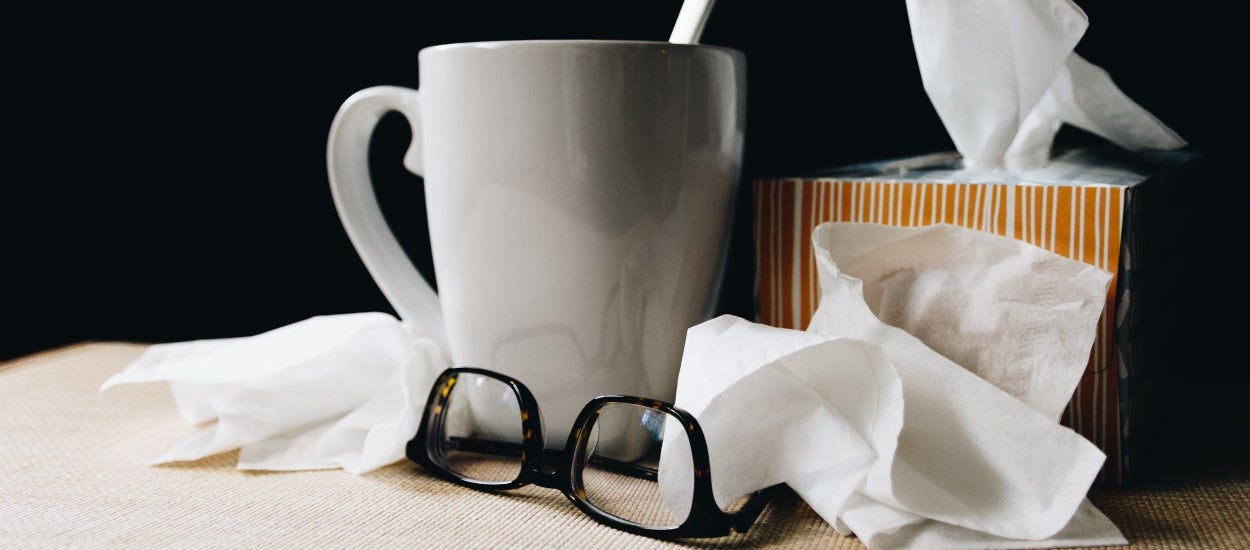 White mug and black reading glasses on a table with a box of tissues