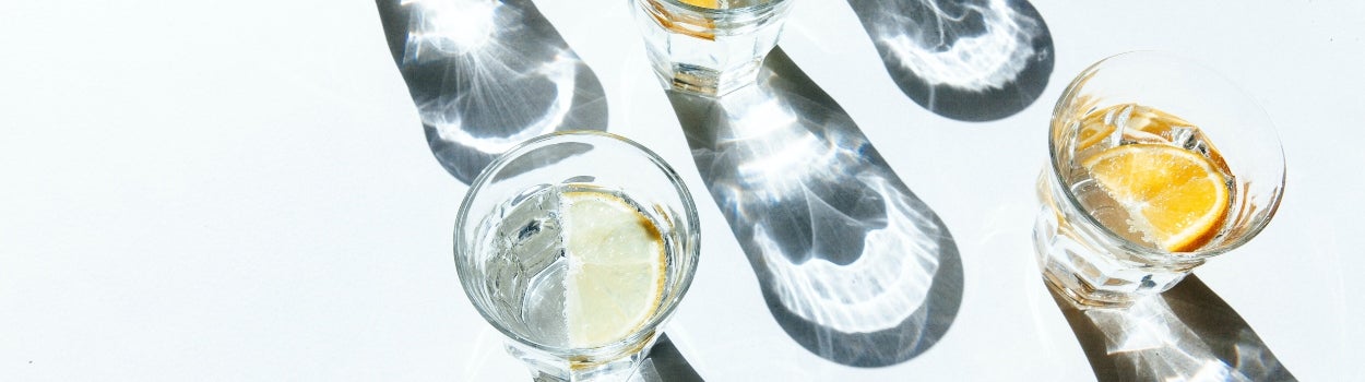 Five clear classes of water with lemon sitting on a white bench, casting shadows from the sun.