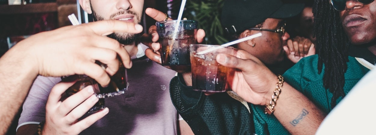 Four men clinking their short glasses of alcohol together in a bar setting.