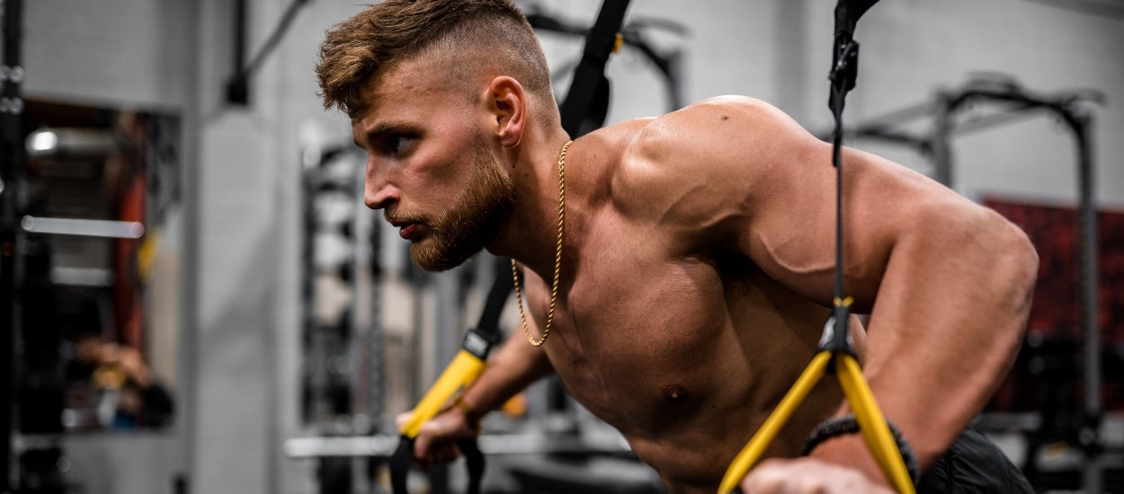 Shirtless fit young man working out in an indoor gym.