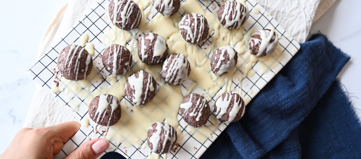 Milk and white chocolate protein balls on a white serving platter with a blue hand towel.