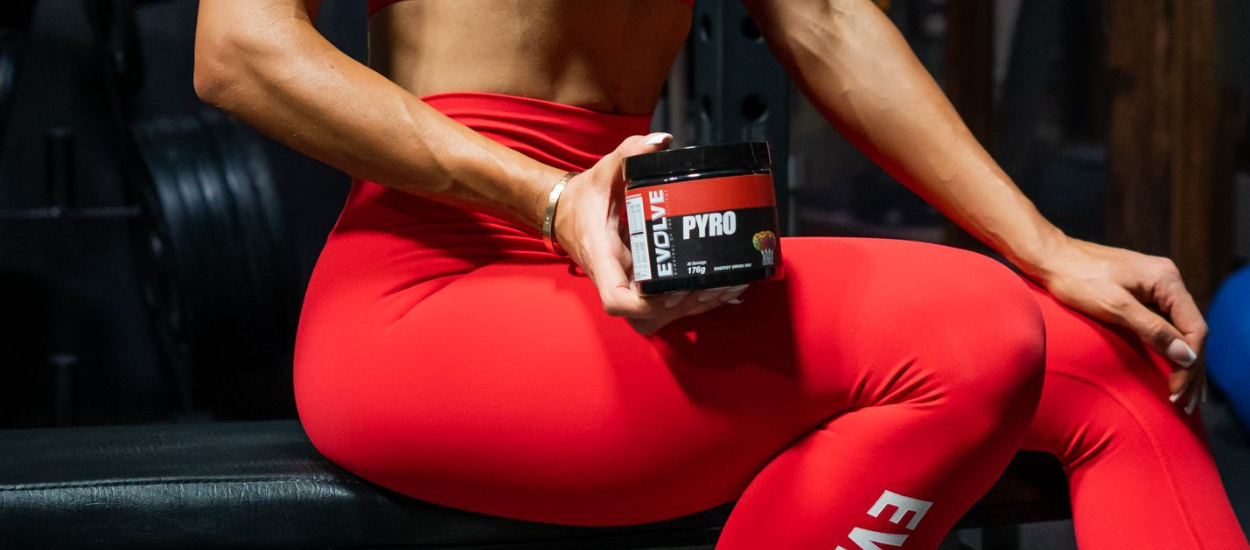 women holding a tub of pre-workout on bench seat at gym