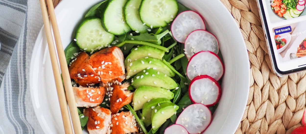 bowl with chopsticks featuring salmon pieces, cucumber, avocado and radishes
