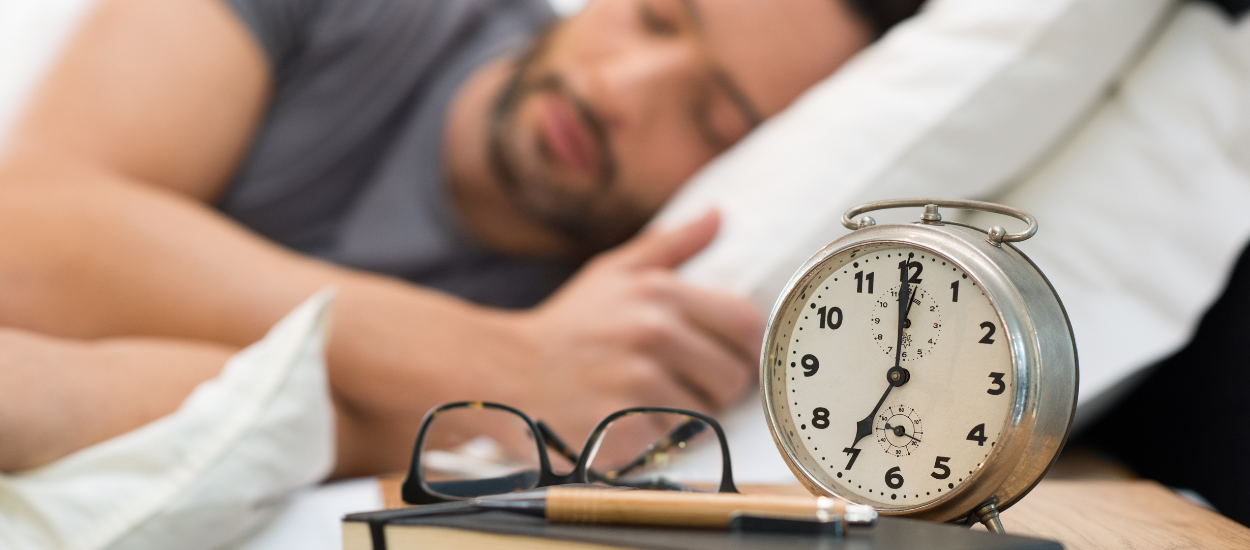 man sleeping in bed with alarm clock on side table